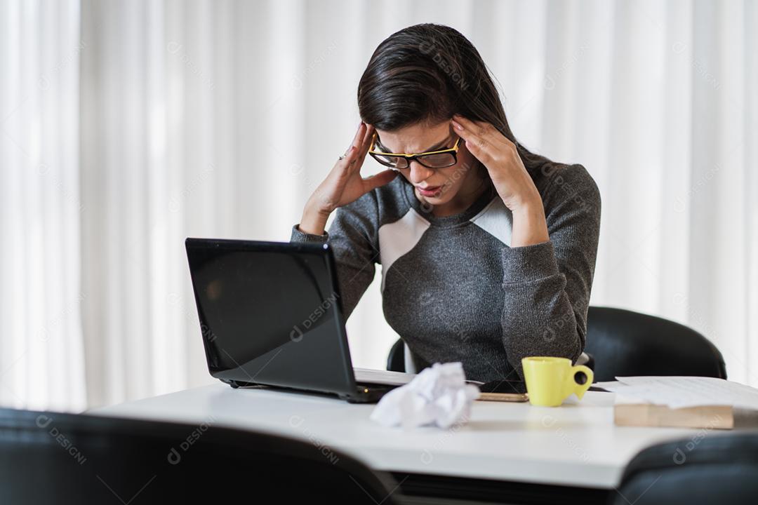 Mulher latina estressada que sofre de enxaqueca com um laptop sentado em uma mesa em casa