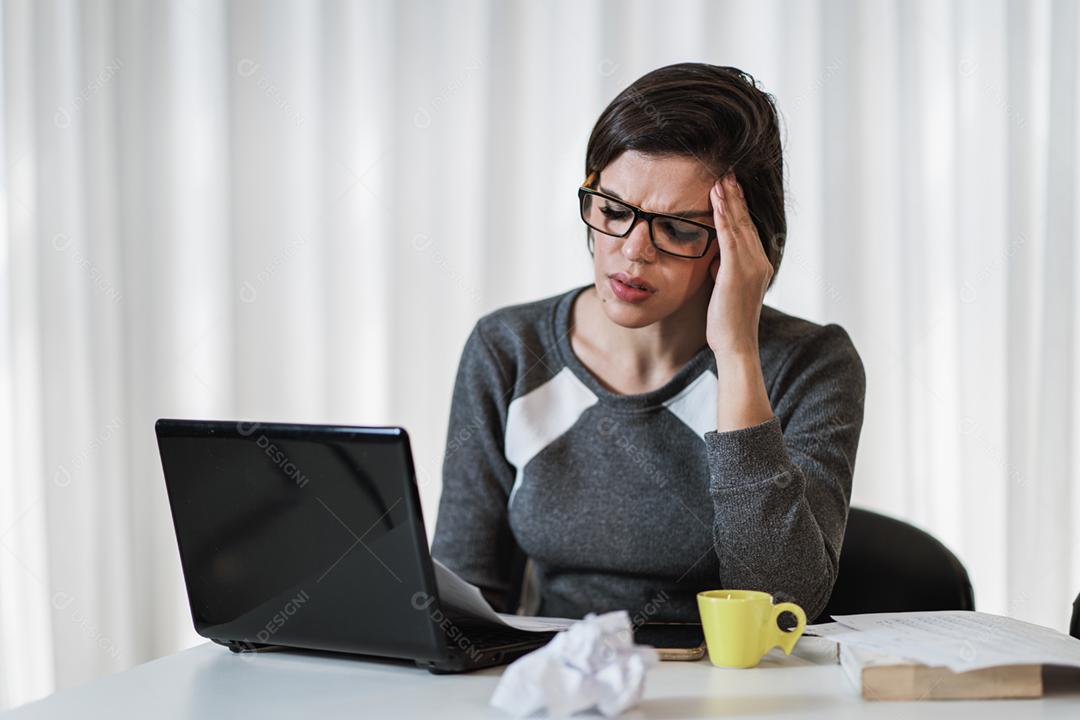 Mulher latina estressada que sofre de enxaqueca com um laptop sentado em uma mesa em casa