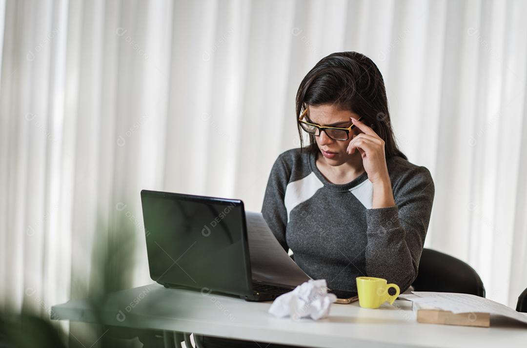 Mulher latina estressada que sofre de enxaqueca com um laptop sentado em uma mesa em casa