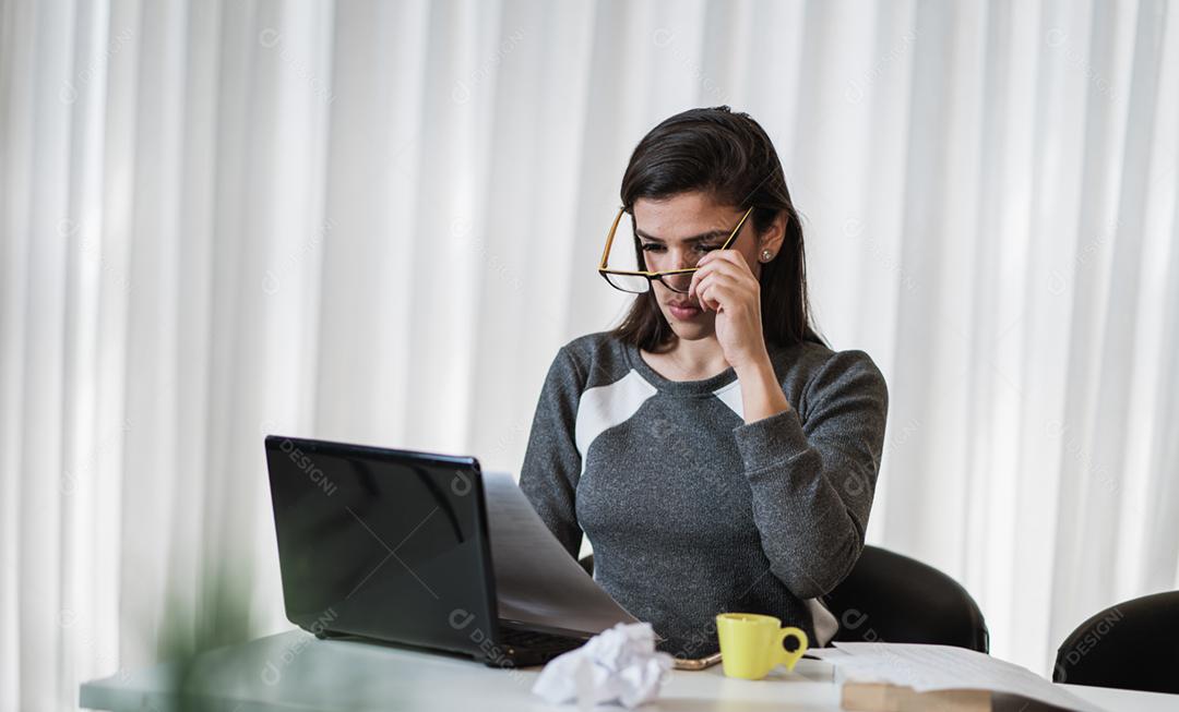 Mulher latina estressada que sofre de enxaqueca com um laptop sentado em uma mesa em casa