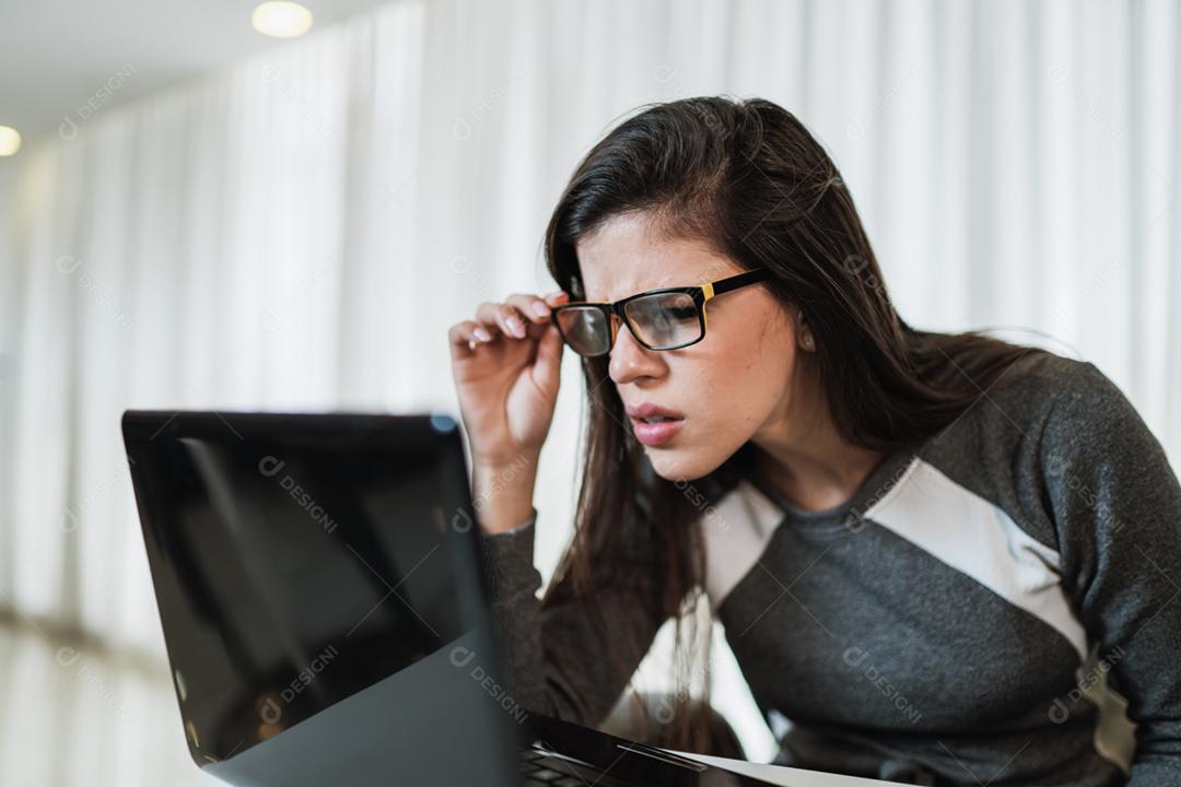 Mulher latina com problemas de visão tentando ler conteúdo online em um laptop em casa.