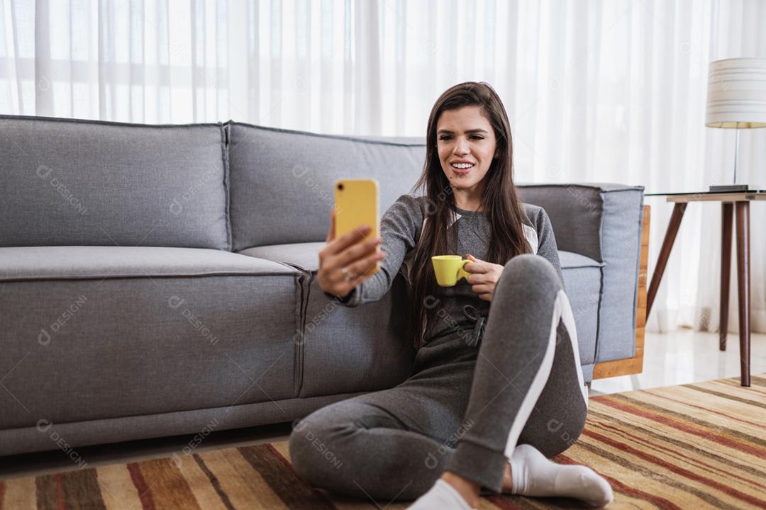 Feliz dama latina relaxa em casa sozinha, sente-se na sala e compartilhe boas notícias nas mídias sociais via celular.