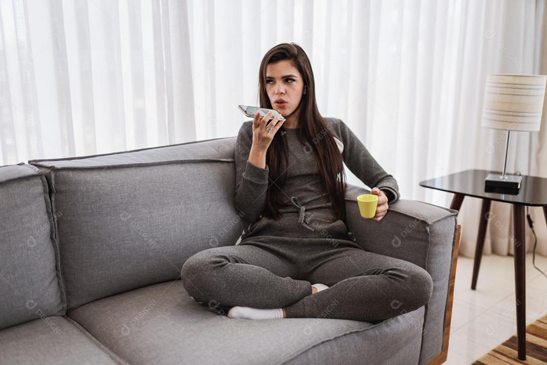 Feliz dama latina relaxa em casa sozinha, sente-se na sala e compartilhe boas notícias nas mídias sociais via celular.