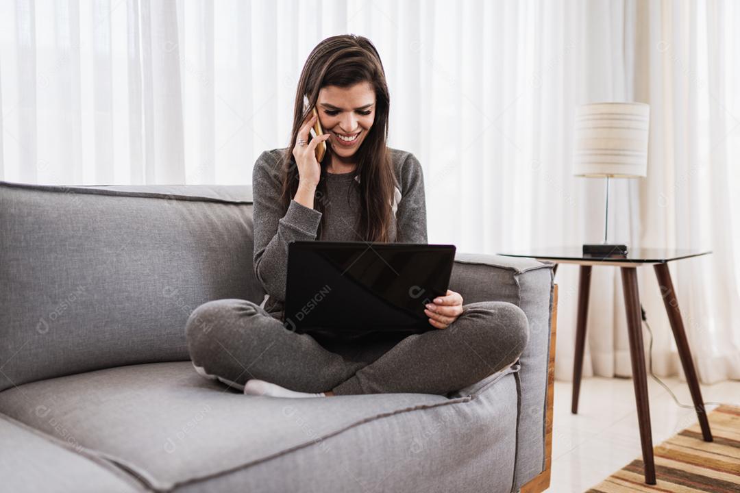 Jovem linda brasileira trabalhando com laptop enquanto está sentado no sofá, trabalhando em casa conceito.