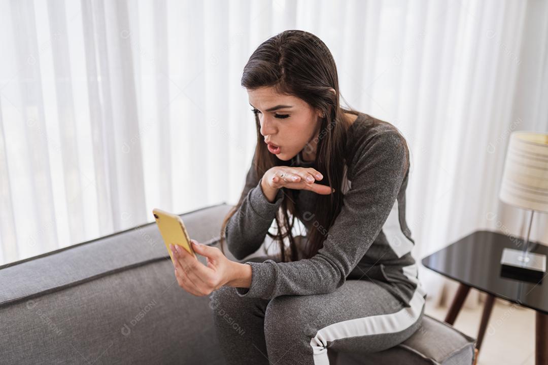 Feliz dama latina relaxa em casa sozinha, sente-se na sala e compartilhe boas notícias nas mídias sociais via celular