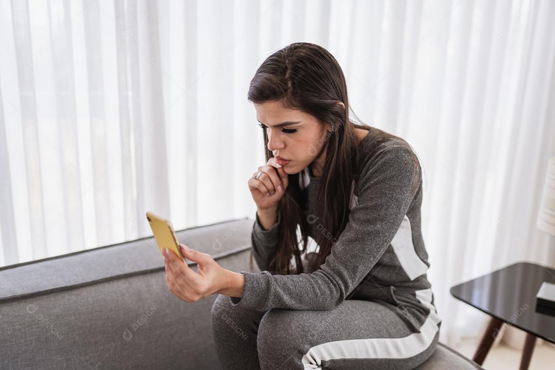 Feliz dama latina relaxa em casa sozinha, sente-se na sala e compartilhe boas notícias nas mídias sociais via celular