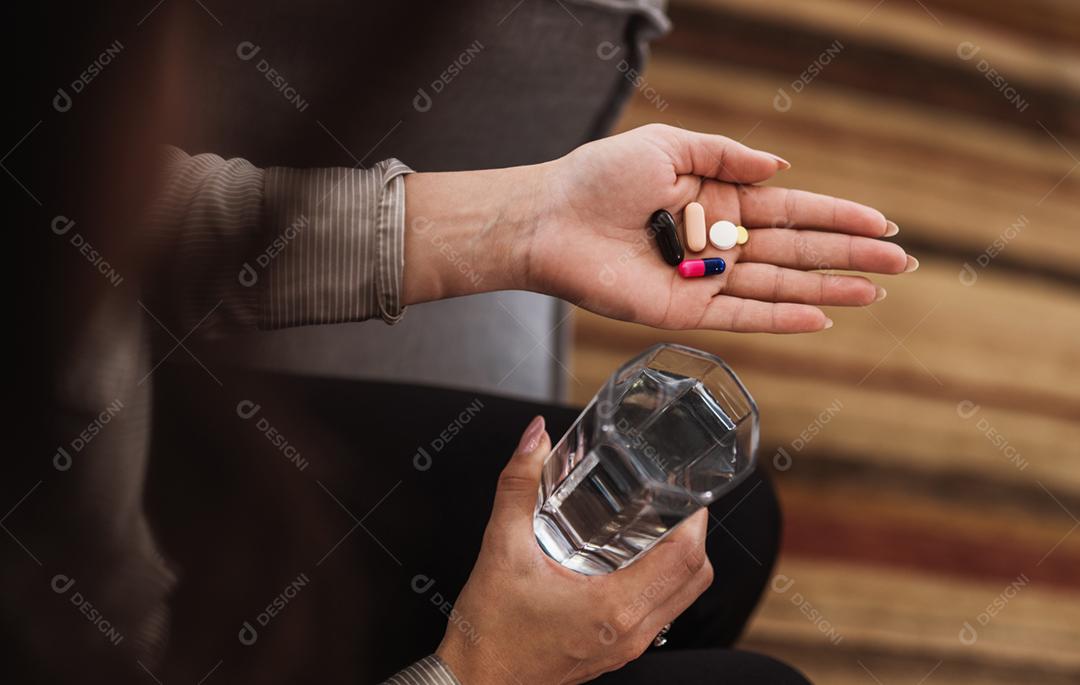 Feche de mulher segurando vários comprimidos, pílulas e copo de água. Tomar vitaminas, medicamentos