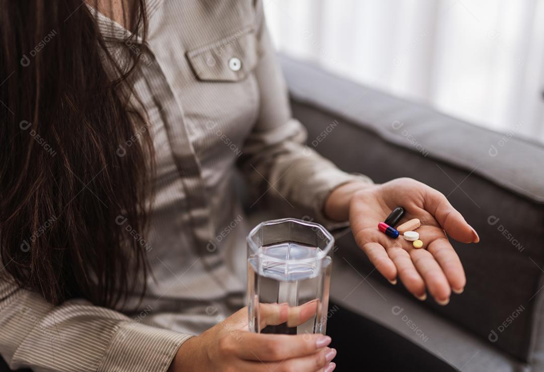 Feche de mulher segurando vários comprimidos, pílulas e copo de água. Tomar vitaminas, medicamentos