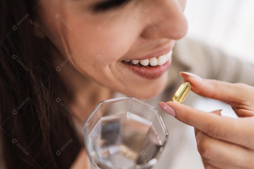 Mulher latina segurando uma cápsula de óleo de peixe Omega 3 em casa.