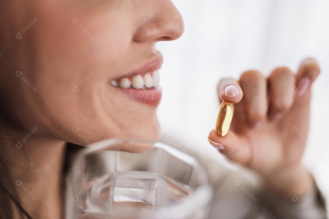 Mulher latina segurando uma cápsula de óleo de peixe Omega 3 em casa.