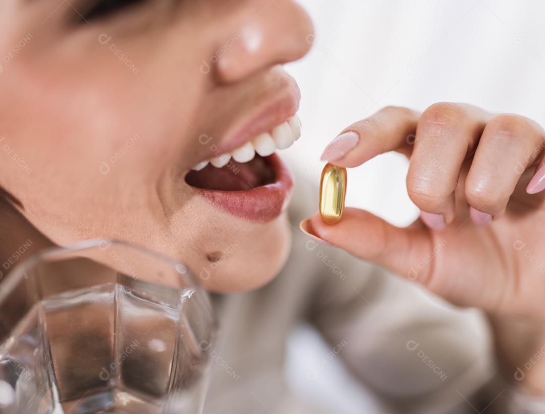 Mulher latina segurando uma cápsula de óleo de peixe Omega 3 em casa.