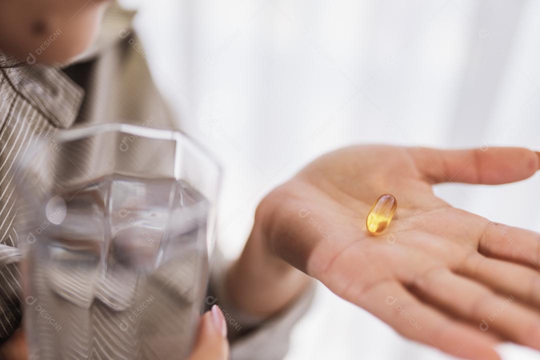 Mulher latina segurando uma cápsula de óleo de peixe Omega 3 em casa.