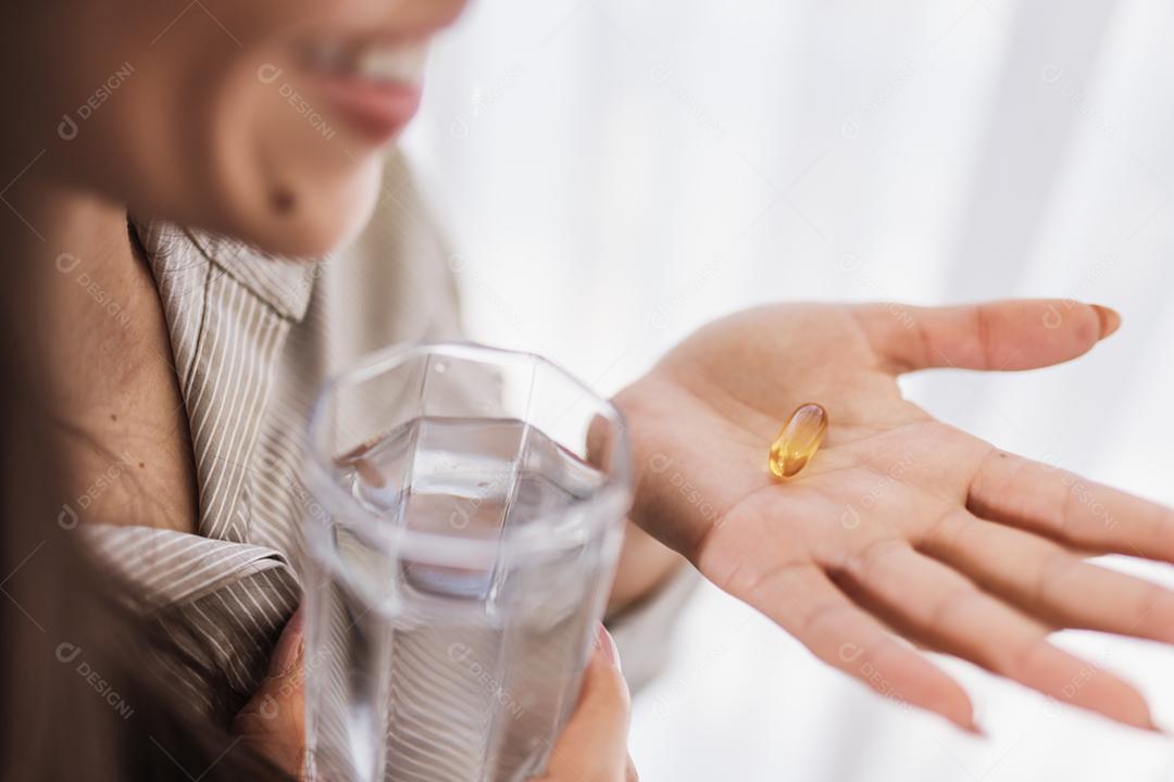 Mulher latina segurando uma cápsula de óleo de peixe Omega 3 em casa.