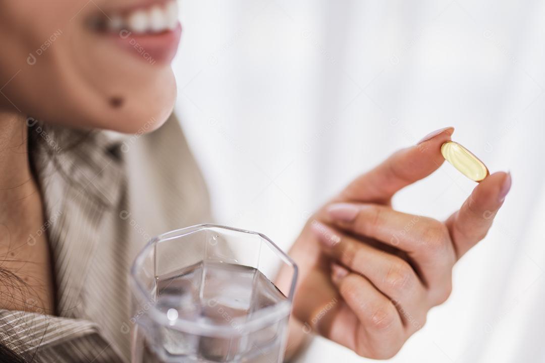 Mulher latina segurando uma cápsula de óleo de peixe Omega 3 em casa.