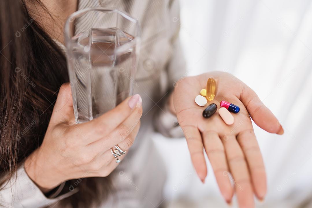 Feche de mulher segurando vários comprimidos, pílulas e copo de água. Tomar vitaminas, medicamentos