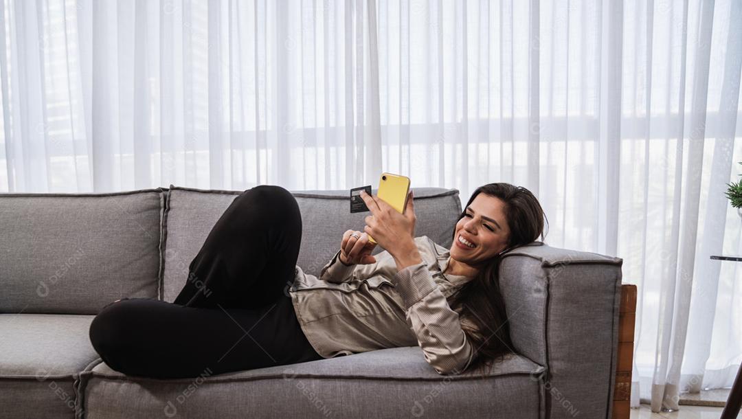 O cliente sorridente da senhora latina segura o cartão de crédito do telefone móvel para fazer compras on-line