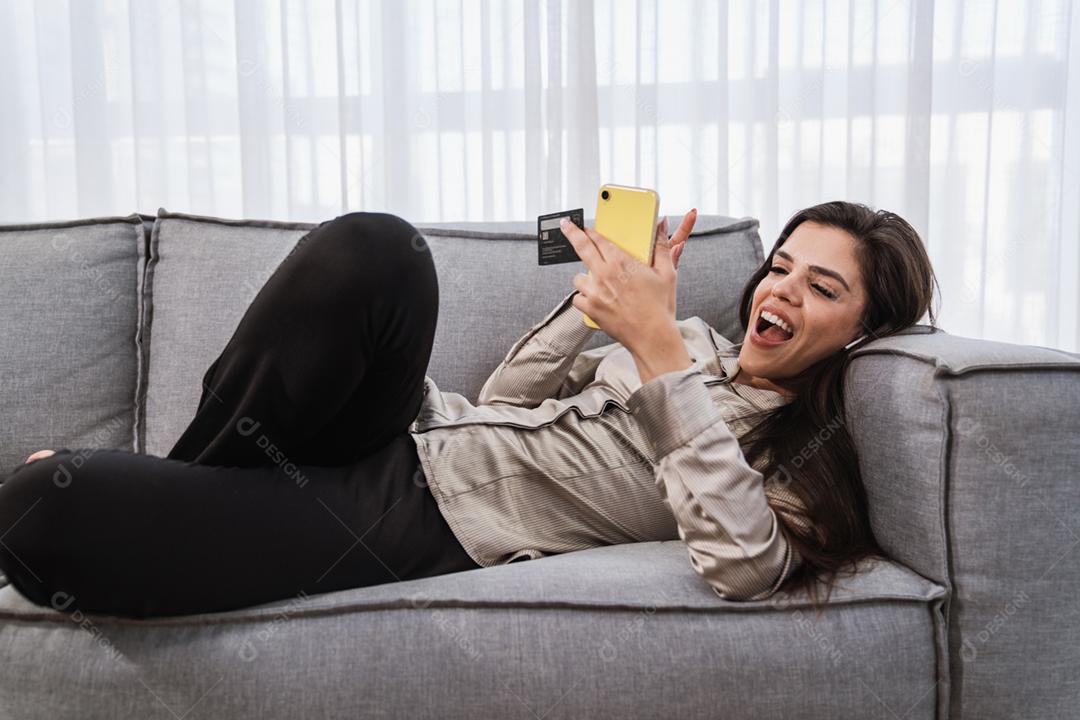 O cliente sorridente da senhora latina segura o cartão de crédito do telefone móvel para fazer compras on-line