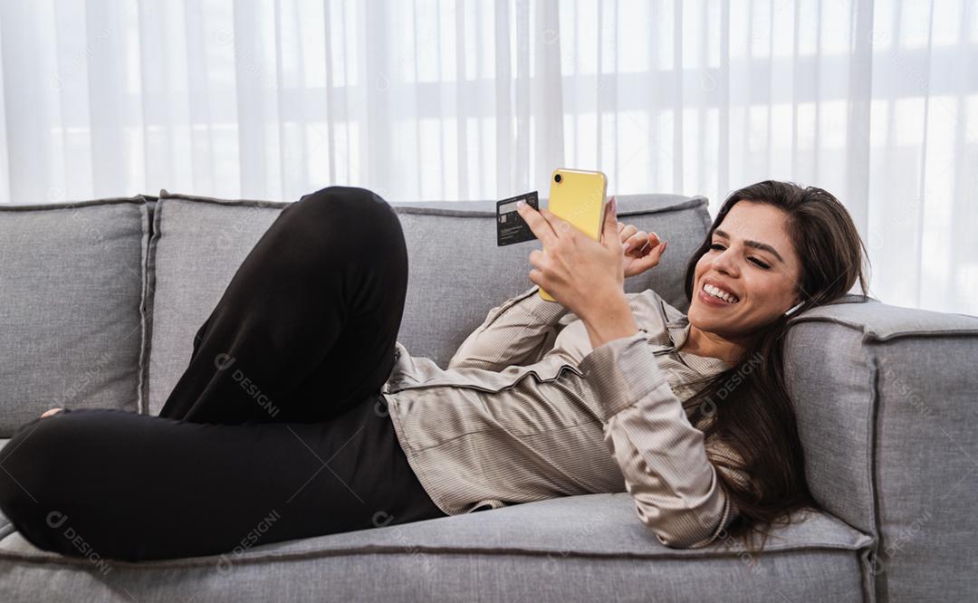 O cliente sorridente da senhora latina segura o cartão de crédito do telefone móvel para fazer compras on-line