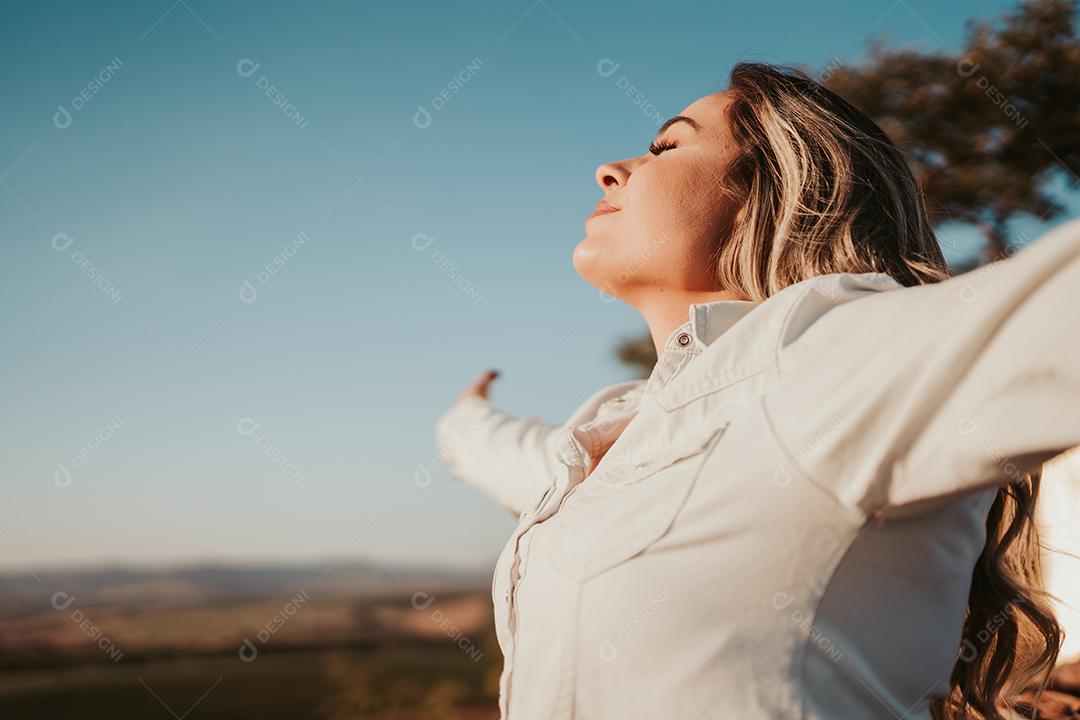 Mulher latina ao pôr do sol respirando ar fresco levantando os braços.