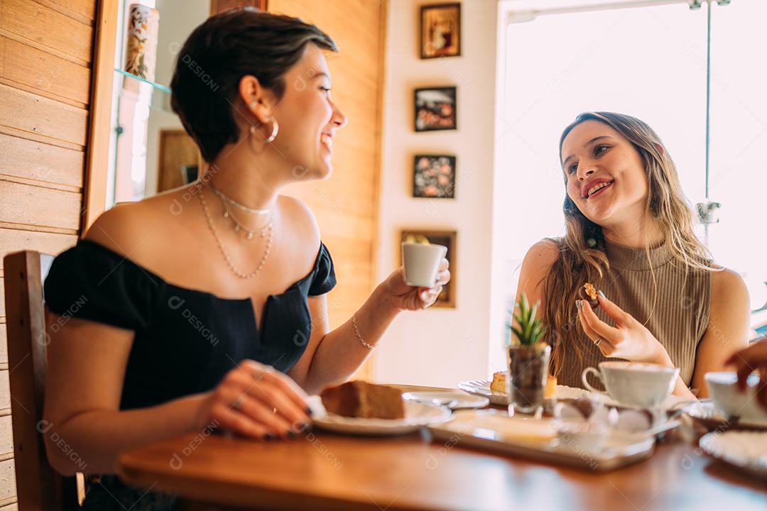 Jovens latinas sentadas em café, tomando café com bolos