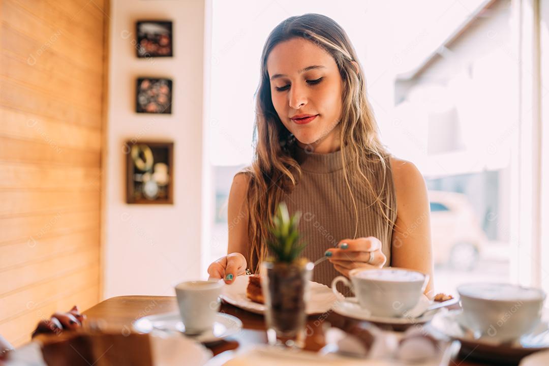Jovem latina sentada em café comendo bolo