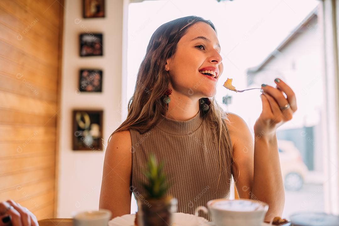 Jovem latina sentada em café comendo bolo