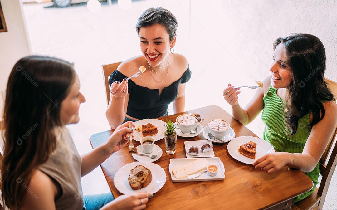 Jovens latinas sentadas em café, tomando café com bolos