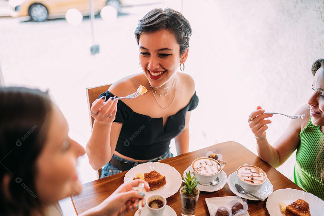 Jovens latinas sentadas em café, tomando café com bolos