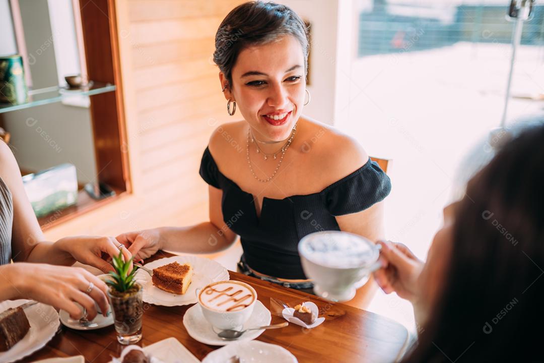 Jovens garotas latinas sentadas no café, tomando café com bolos e ouvindo a história de vida engraçada de seu amigo