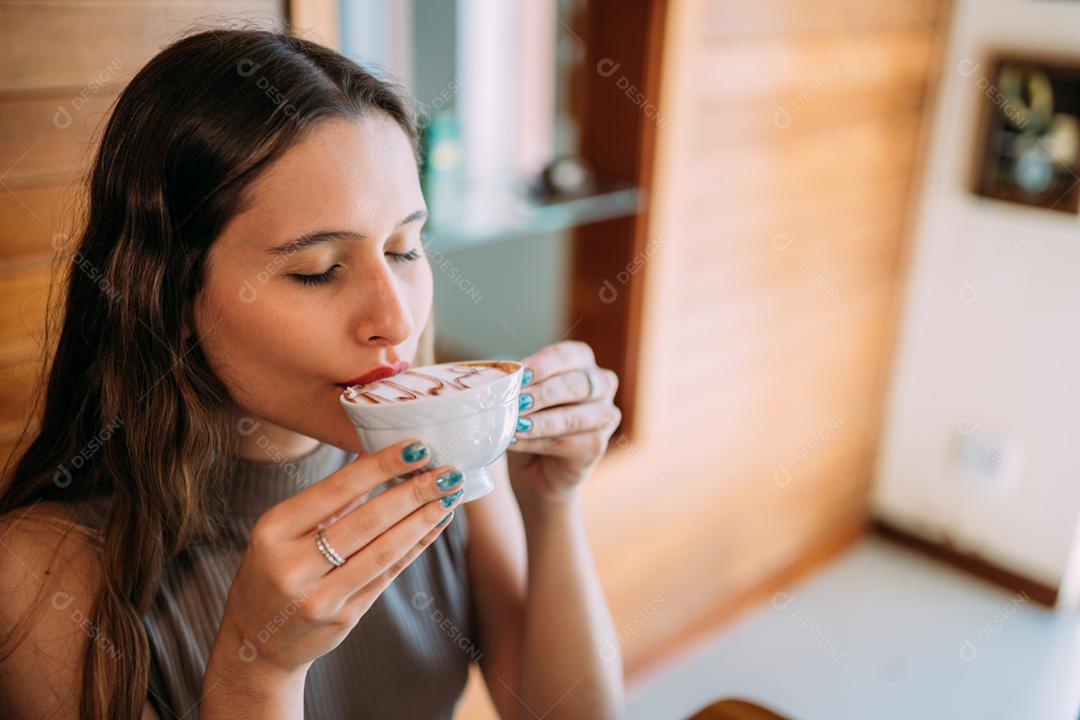 Jovem e linda mulher latina feliz desfrutando de cappuccino em um café de rua
