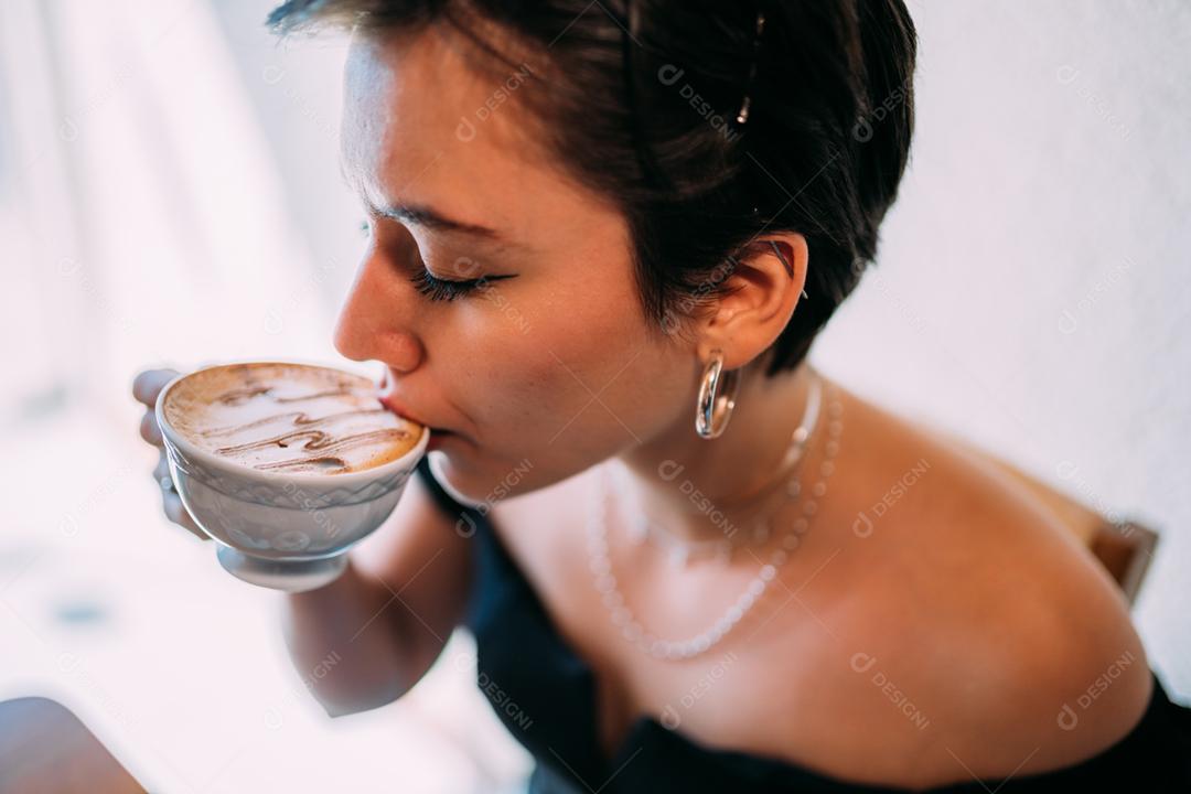 Jovem e linda mulher latina feliz desfrutando de cappuccino em um café de rua