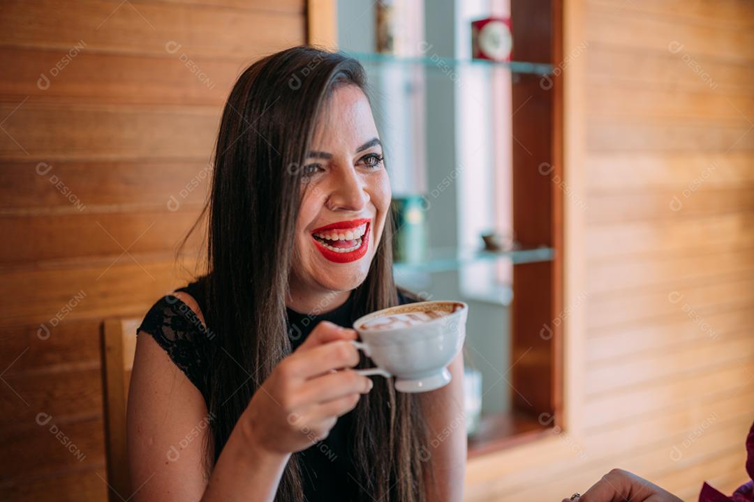 Jovem e linda mulher latina feliz desfrutando de cappuccino em um café de rua