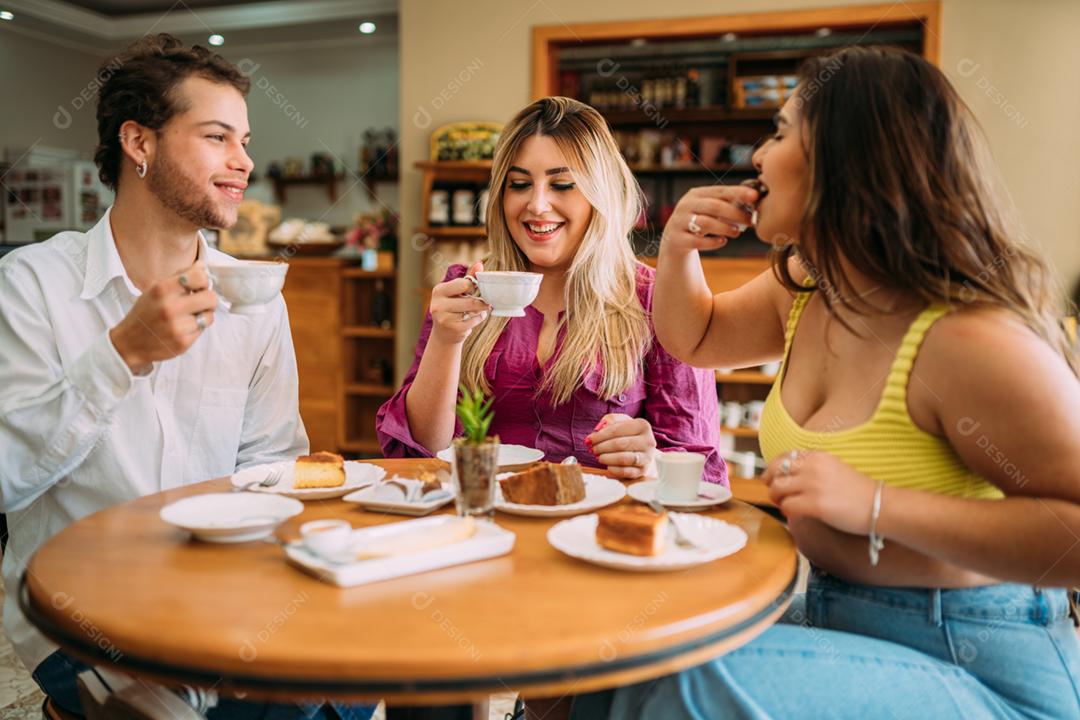 Jovens latinos sentados no café, tomando café com bolos e ouvindo a história de vida engraçada de seu amigo
