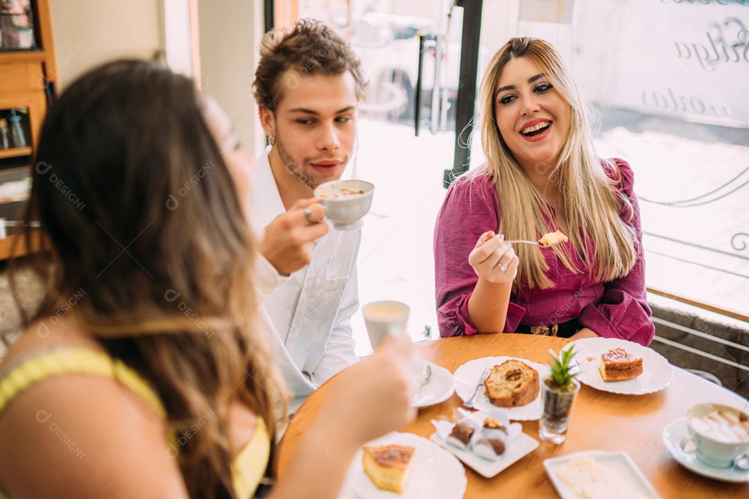 Jovens latinos sentados no café, tomando café com bolos e ouvindo a história de vida engraçada de seu amigo