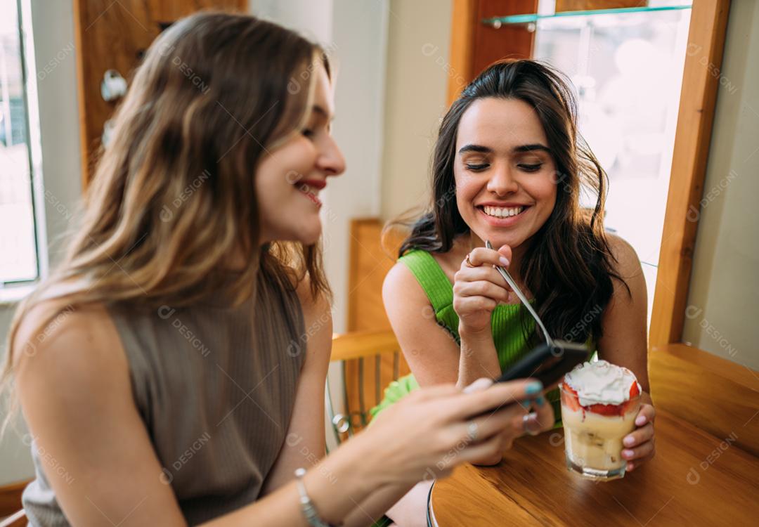 Animadas lindas duas mulheres latinas assistem a um vídeo engraçado no celular moderno, têm expressões