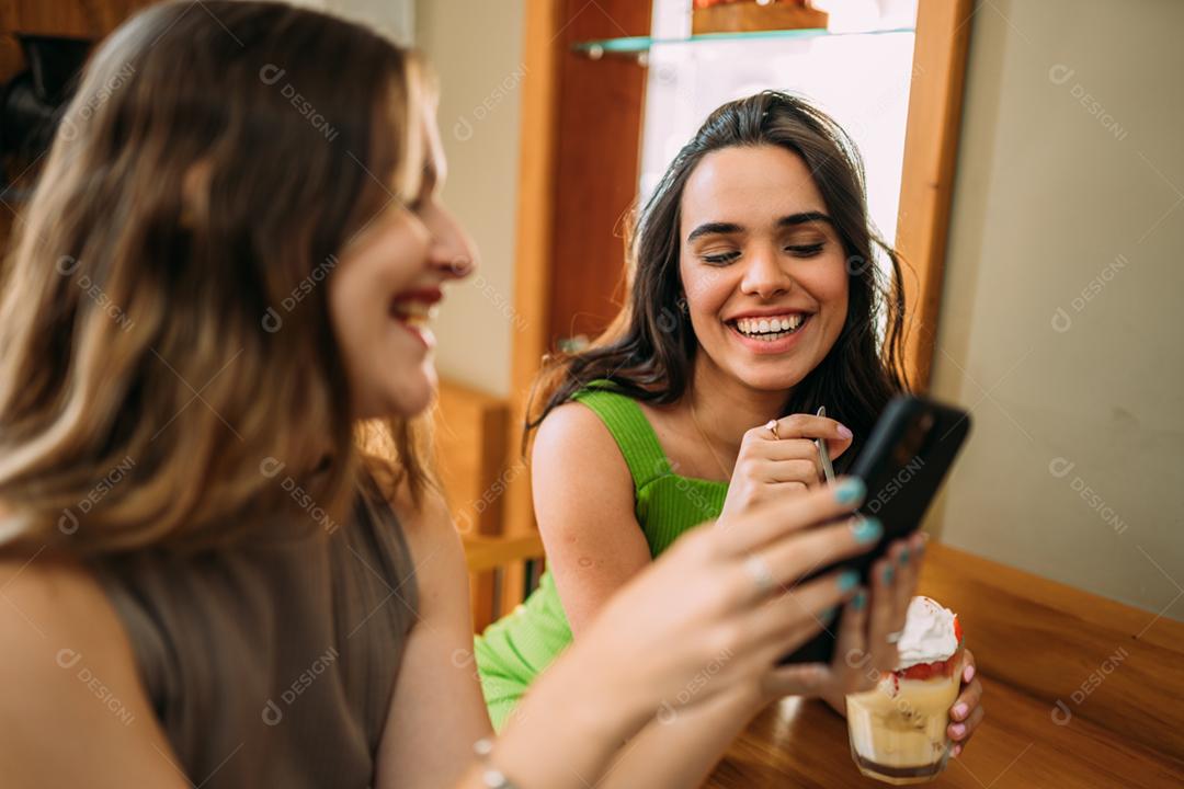 Animadas lindas duas mulheres latinas assistem a um vídeo engraçado no celular moderno, têm expressões