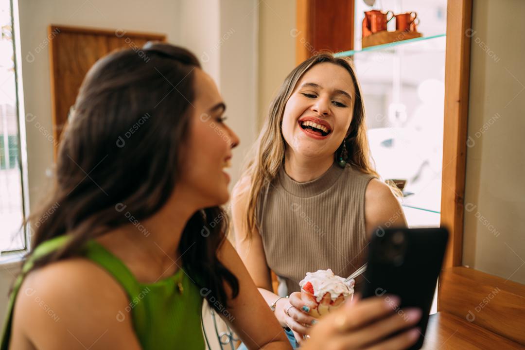 Animadas lindas duas mulheres latinas assistem a um vídeo engraçado no celular moderno, têm expressões