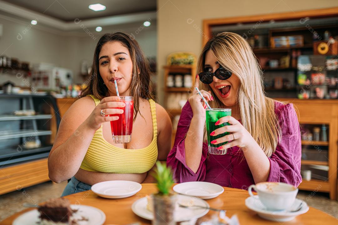 Jovens garotas latinas plus size sentadas no café ouvindo a história de vida engraçada de seu amigo
