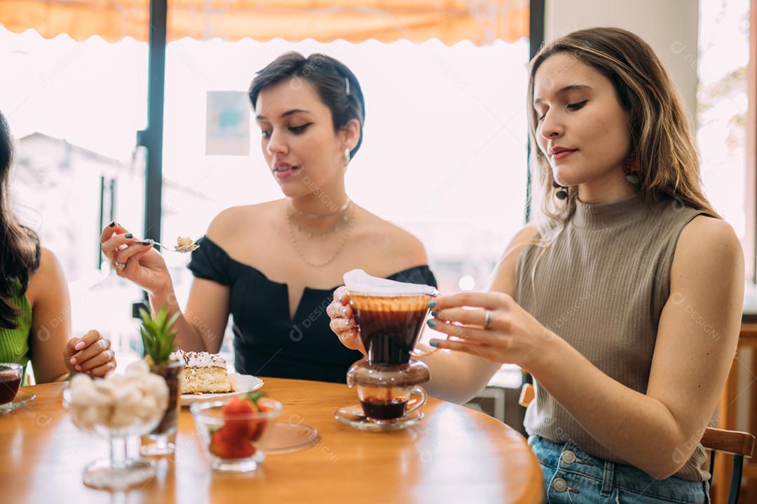 Jovens garotas latinas sentadas no café tomando café e comendo bolo