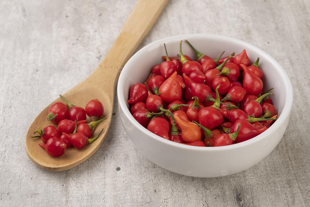 Bico de pimenta vermelha em uma tigela e colher sobre mesa de madeira