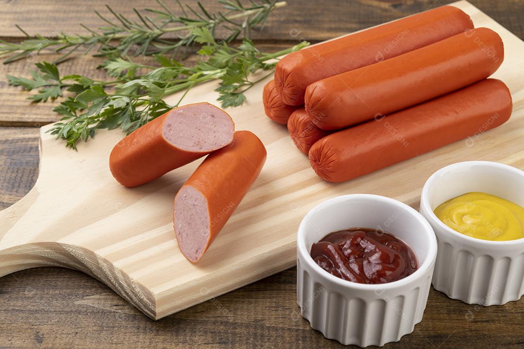 Salsichas e fatias sobre uma tábua de madeira com ketchup e mostarda