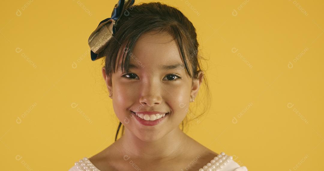 Linda garota asiática sentada no fundo amarelo. Feliz menina asiática sorrindo.