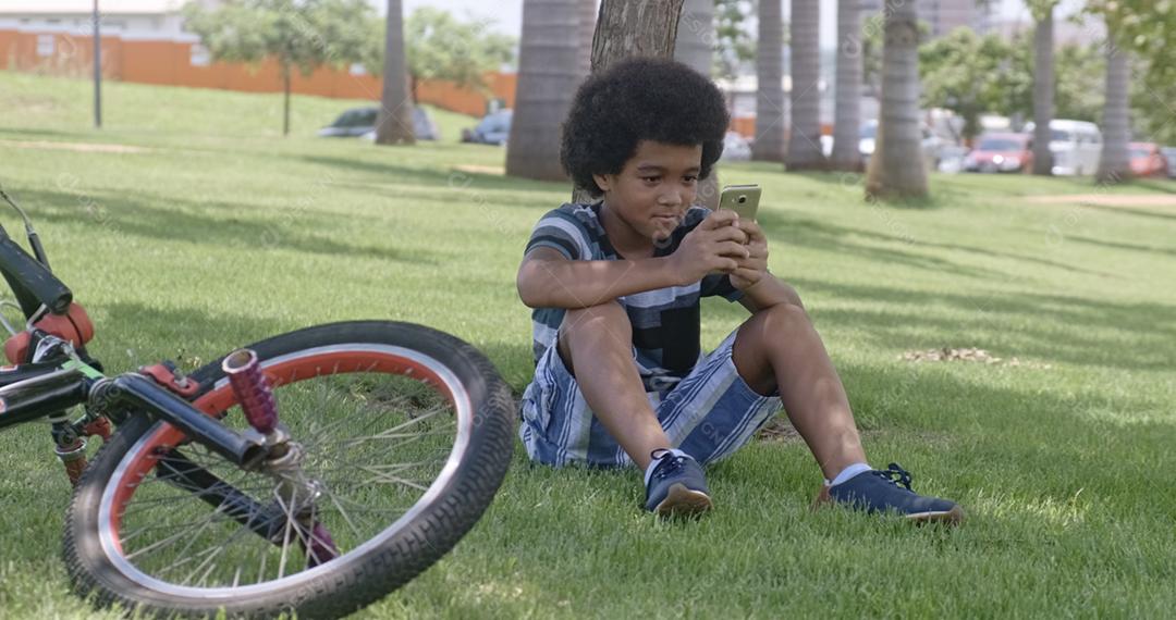 O jovem senta-se na grama no jardim e usando smartphone.