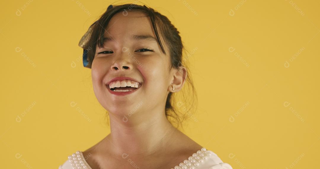 Linda garota asiática sentada no fundo amarelo. Feliz menina asiática sorrindo.