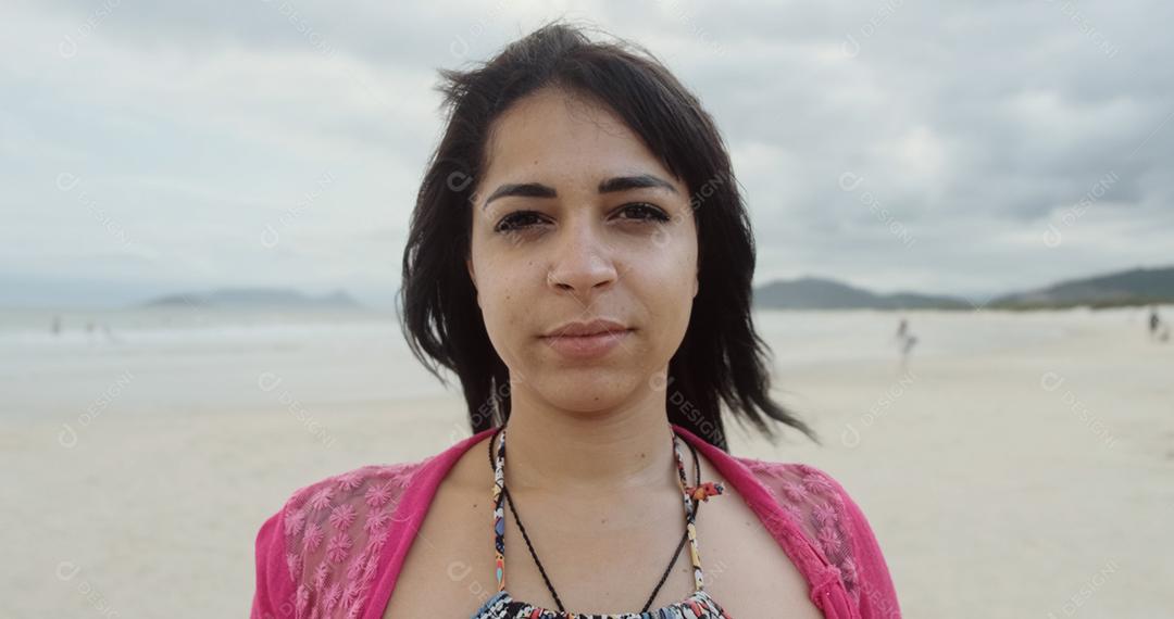 Mulher latina olhando para a câmera e sorrindo na praia no Brasil.