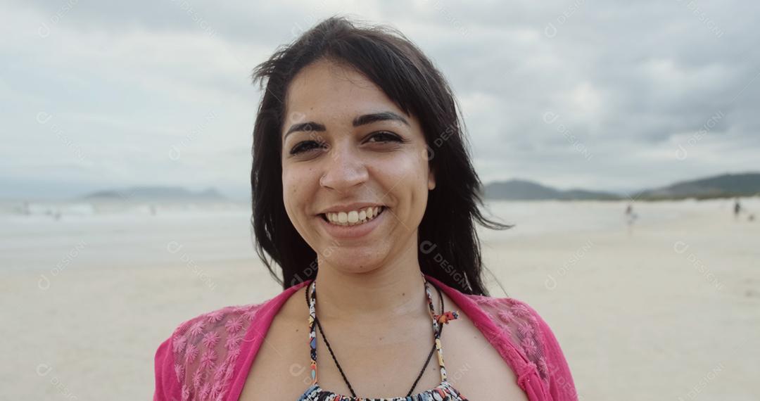 Mulher latina olhando para a câmera e sorrindo na praia no Brasil.