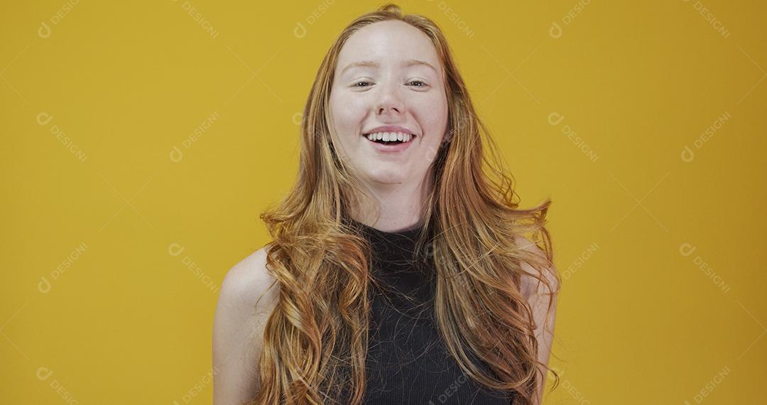 Linda garota ruiva alegre sorrindo rindo olhando para a câmera sobre fundo amarelo.