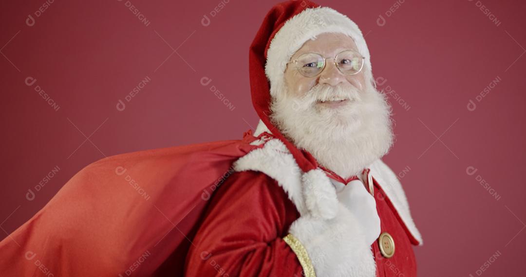 Verdadeiro Papai Noel com um fundo vermelho, usando óculos, luvas e um chapéu olhando de lado.