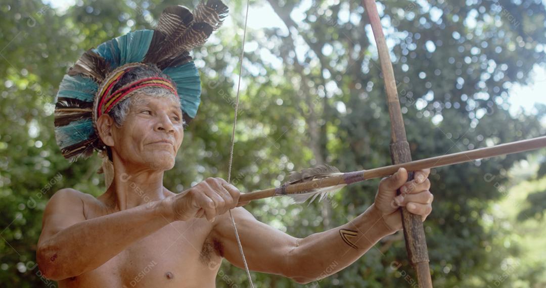 Índio da tribo Pataxó, com cocar de penas e arco e flecha. Índio brasileiro idoso olhando para a direita.
