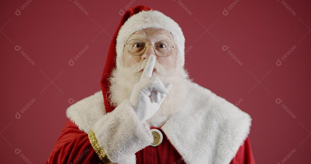 Papai Noel mantendo o dedo indicador pela boca e olhando para a câmera. Shh! Guarde segredo